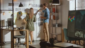 2 people facing a wall with their accessibility design story board posted on the wall