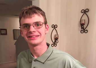 Photograph of Noah, smiling, wearing glasses and his green Publix employee shirt
