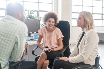 Three coworkers seated and chatting in the office. One is in a wheelchair.