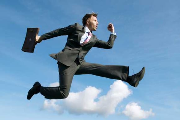 a businessman in a suit with a briefcase leaping into a blue, partly cloudy sky