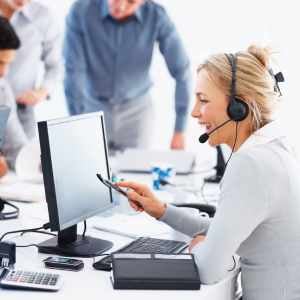 a customer service rep, smiling, on a call, looking at her monitor, with her teammates in the background