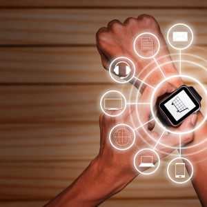 a hand with a smartwatch on it, the other hand touching it, with icons for various internet things imposed over it in white