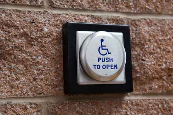 a large silver handicap door open button on a brick wall