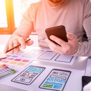 a man looking at color sketches of an app while holding his phone and looking at it