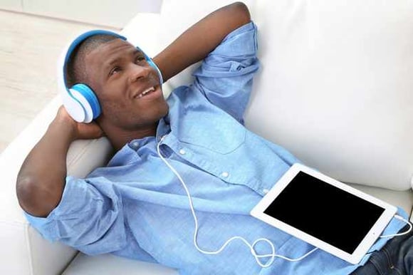 a man lounging on the couch with headphones on listening to his tablet