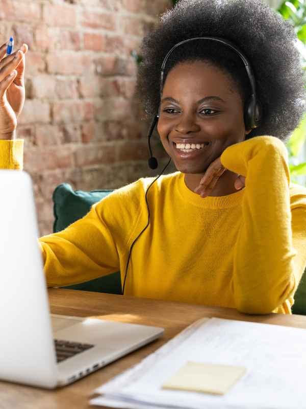 a woman in a bright yellow sweater with headphones on smiling as she watches her laptop (600 × 800 px)