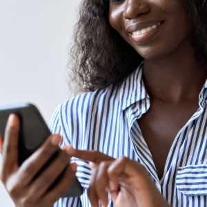 a woman in a striped shirt holding her phone in one hand and using her finger to navigate it with the other