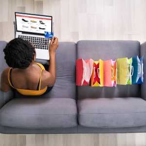 a woman sitting on a couch browsing an online shopping site, holding her credit card, and several shopping bags next to her