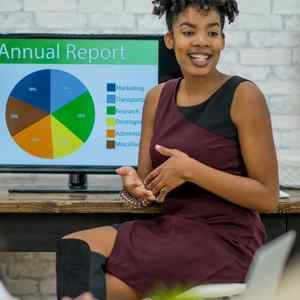 a-lady-sitting-while-turned-to-her-audience-with-a-presentation-on-her-computer-monitor