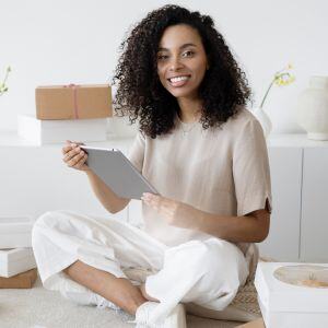 a-woman-sitting-cross-legged-on-the-floor-holding-her-tablet