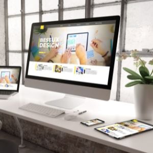 a_clean_desk_with_a_laptop_and__a_monitor_and_a_mobile_phone_and_a_tablet_on_it_all_displaying_a_website_with_the_heading_Best_UX_Design