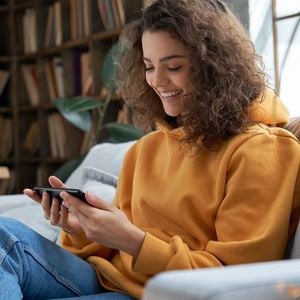 female_smiling_sitting_on_a_couch_watching_a_video_on_her_phone