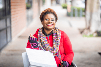 Woman with a big smile in a wheelchair holding a shopping bag on a city sidewalk