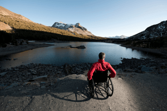 A man using a wheelchair views the shore of a lake