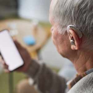 man-holding-smartphone-with-hearing-aid-in-his-ear