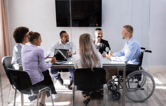 Group of six coworkers around a meeting table, one of whom is in a wheelchair