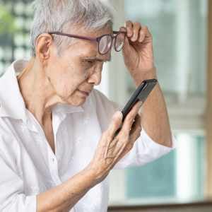 woman-holding-smartphone-squinting-at-it-pulling-her-glasses-up