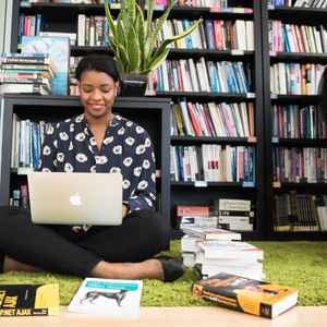 women_sitting_on_the_ground_with_her_laptop_sorrounded_by_books_on_the_floor_in_front_of_a_bookshelf