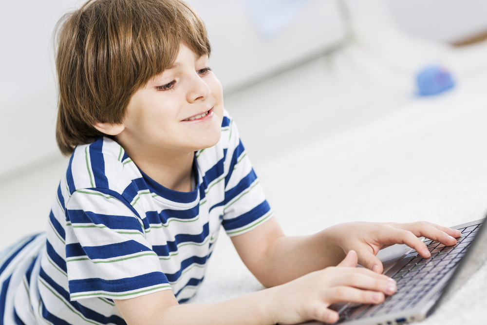 Boy wearing a striped shirt, smiling, typing on a laptop.